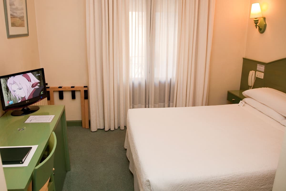 Une chambre d’hôtel avec un lit, un bureau avec un ordinateur, un téléphone et une fenêtre avec des rideaux.