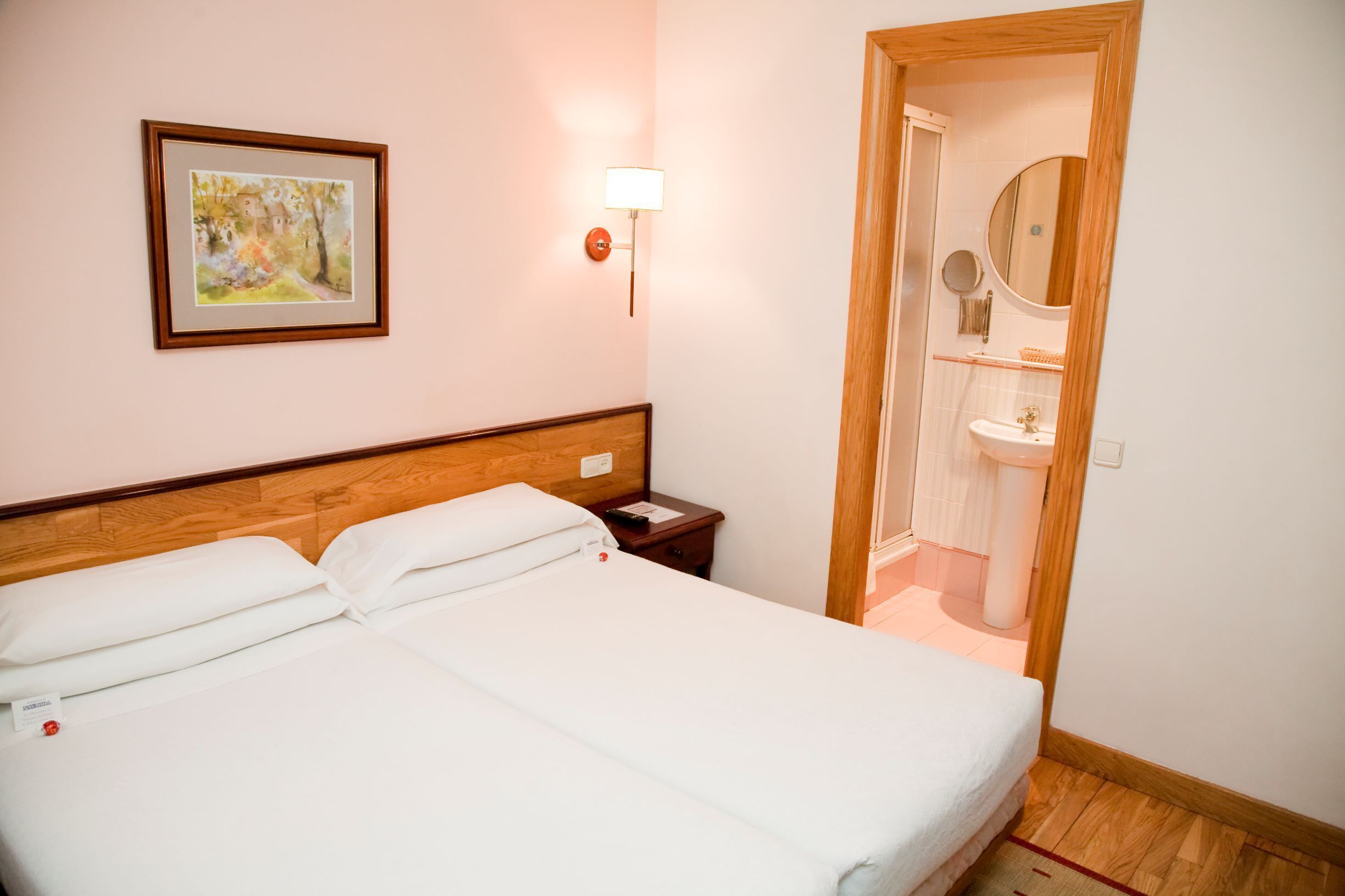 A neatly made bed with white linens, a wooden headboard, a bedside table with a lamp, and a framed picture on the wall.