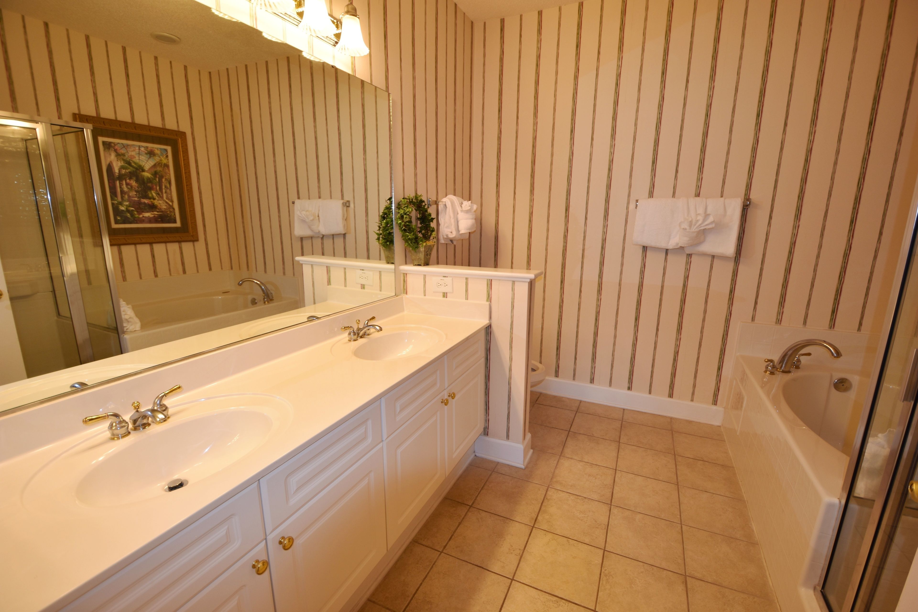 A bathroom with two sinks, a large mirror, a bathtub, and striped wallpaper.