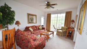 A living room with a sofa, chairs, a coffee table, a ceiling fan, and a large window with curtains. - 123 Harbour Cove (North Myrtle Beach)