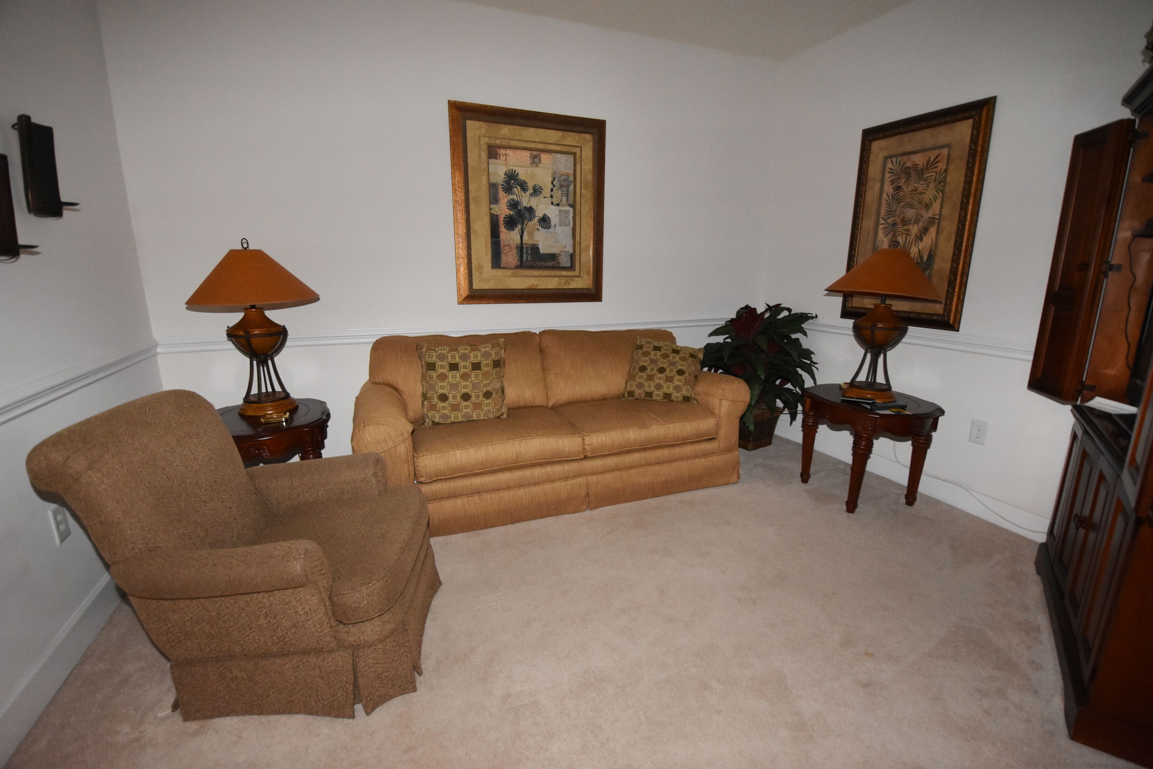 A living room with a brown sofa, two side tables with lamps, a brown armchair, and two framed pictures on the wall.
