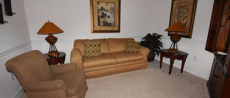 A living room with a brown sofa, two side tables with lamps, a brown armchair, and two framed pictures on the wall.
