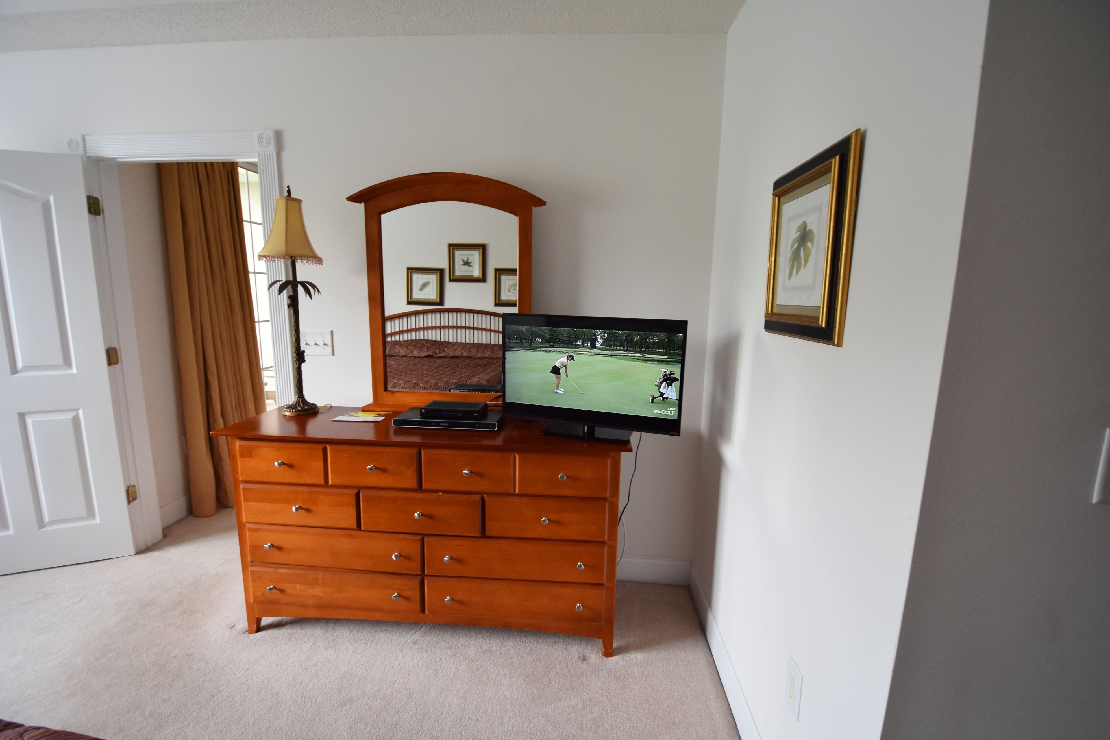 Een kamer met een houten dressoir, een televisie waarop een golfwedstrijd te zien is, een lamp en lijstjes met foto's aan de muur.