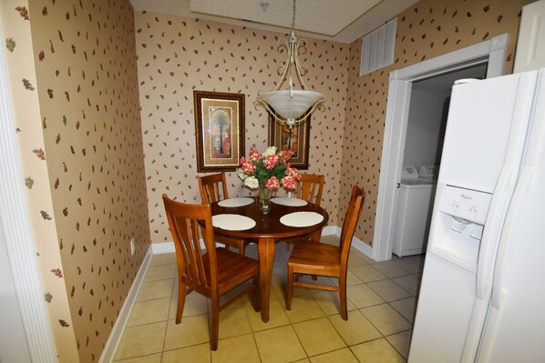 Un comedor con mesa y sillas de madera, una araña y un refrigerador.