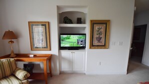 A living room with a television on a stand, a sofa, a table, and framed pictures on the wall. - 123 Harbour Cove (North Myrtle Beach)