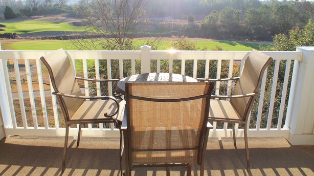 Un balcón con sillas de mimbre y una mesa, con vistas a un campo de golf.