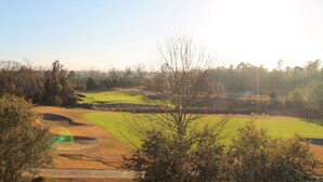 Un campo de golf con búnkeres de arena, cielo despejado y árboles en primer plano.