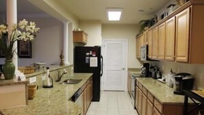Una cocina con encimeras de granito, armarios de madera, un refrigerador negro y una puerta blanca al fondo.