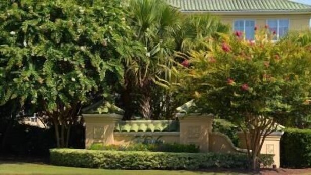 Una casa con jardín cuidado, muro de piedra y un gran árbol de flores rosadas.