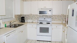 A kitchen with white cabinets, a microwave, an oven, a sink, and a refrigerator. - 112 River Crossing (North Myrtle Beach)