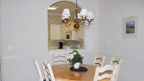 A dining room with a round wooden table, six chairs, a chandelier, and a potted plant. - 112 River Crossing (North Myrtle Beach)