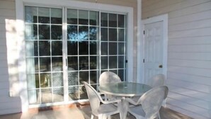 A patio with a round table and four chairs, a sliding glass door, and a white exterior wall. - 1515 The Havens (North Myrtle Beach)