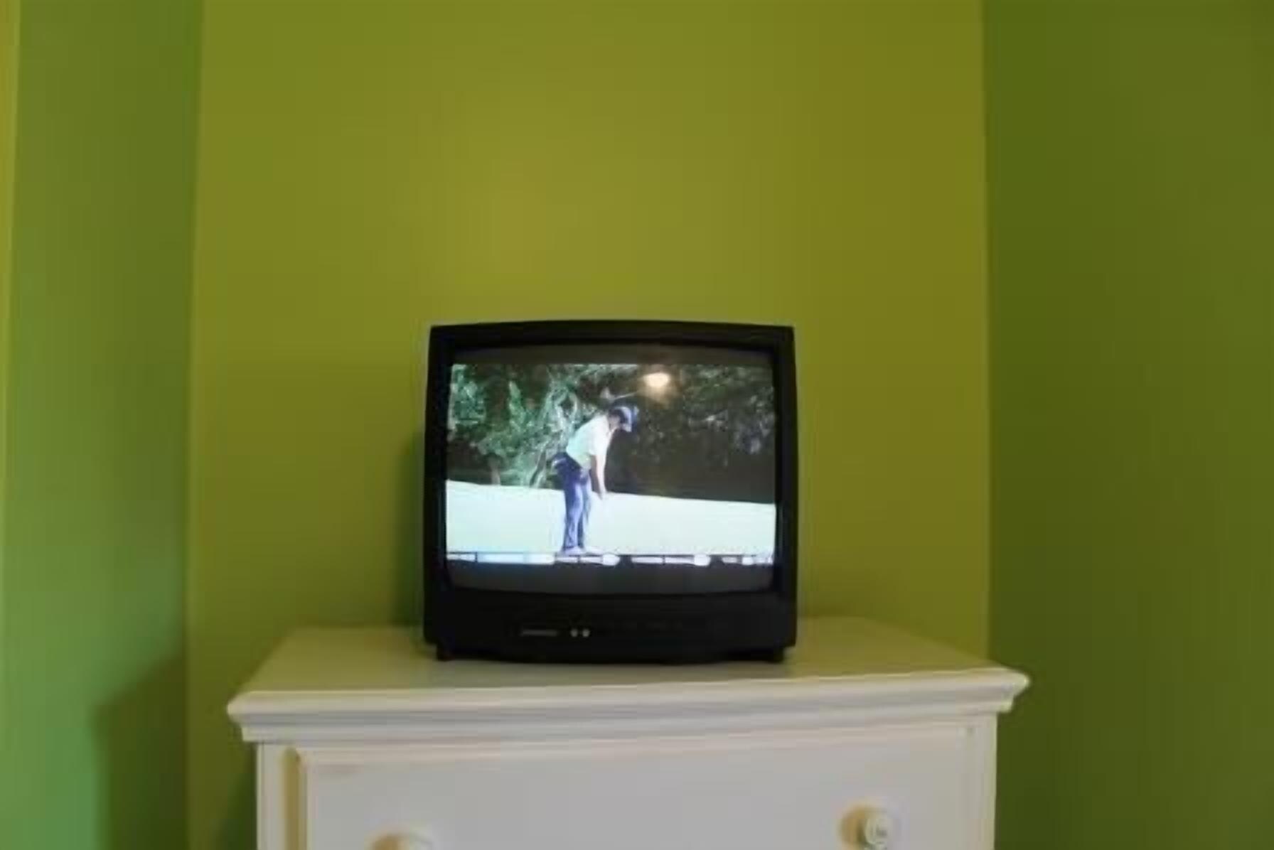 A television on a white cabinet against a green wall.