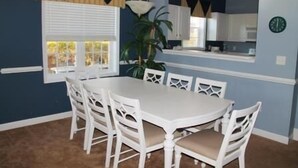 A dining area with a white table and chairs, a potted plant, and a clock on the wall. - 1515 The Havens (North Myrtle Beach)