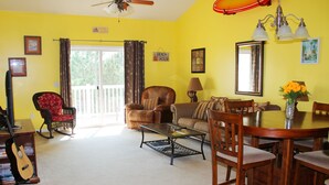A living room with a sofa, chairs, a coffee table, a dining table with chairs, a guitar, and a balcony with curtains. - 1534 Willow Bend (North Myrtle Beach)