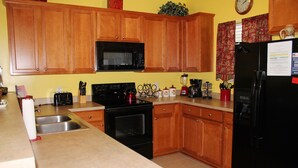 A kitchen with wooden cabinets, a black microwave, a stove, and a refrigerator. - 1534 Willow Bend (North Myrtle Beach)
