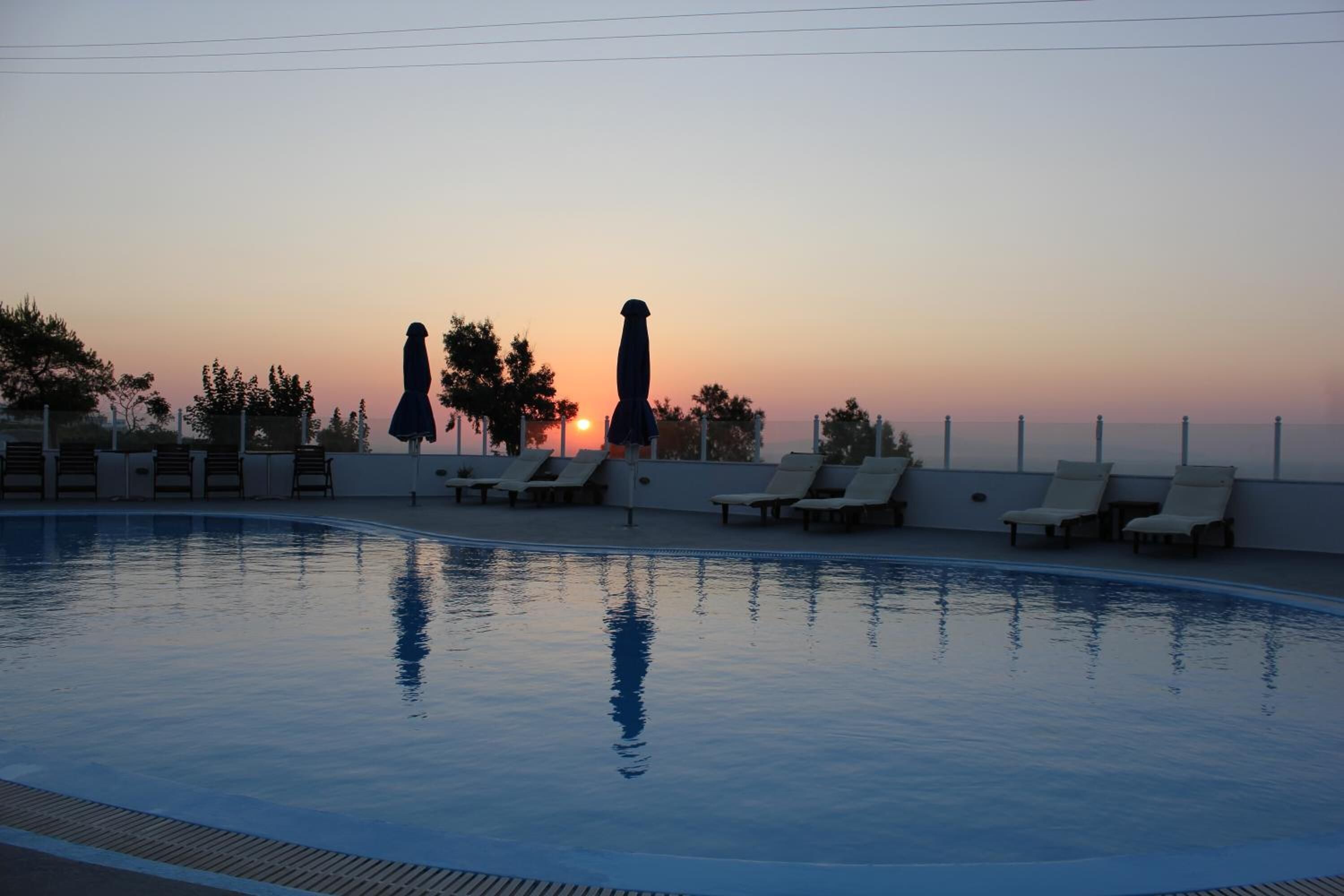 A swimming pool with lounge chairs and umbrellas, set against a sunset sky.