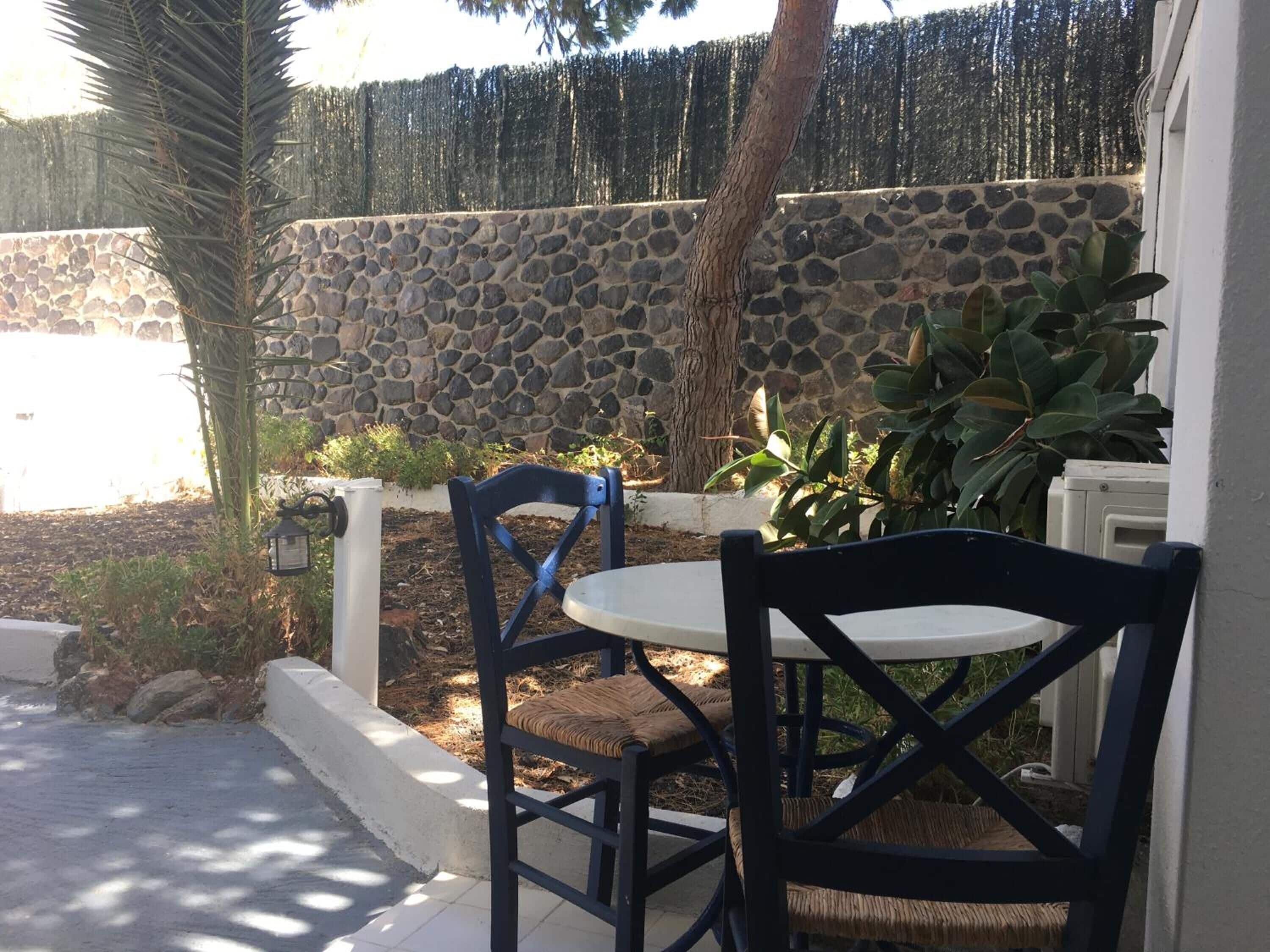 Un patio con dos sillas, una mesa, un muro de piedra y una palmera.