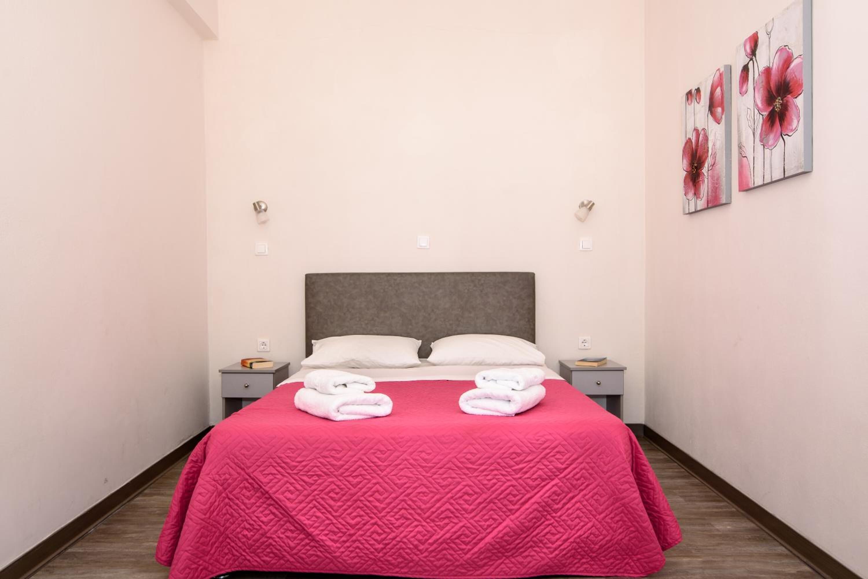 A neatly made bed with a pink quilt, two pillows, and folded towels on the nightstands.