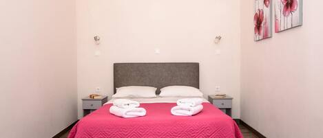 A neatly made bed with a pink quilt, two pillows, and folded towels on the nightstands.