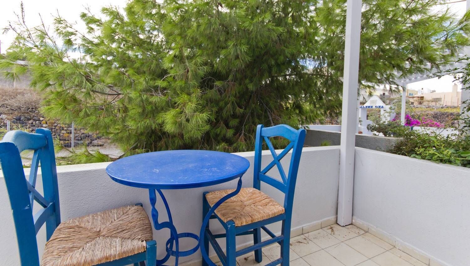 Un petit espace extérieur aménagé avec une table ronde et deux chaises bleues dont les assises sont en osier tressé.
