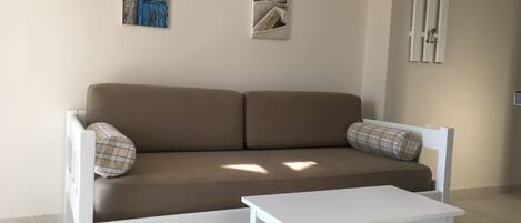 A white sofa with two plaid pillows, a white coffee table, and two wall-mounted decorations.