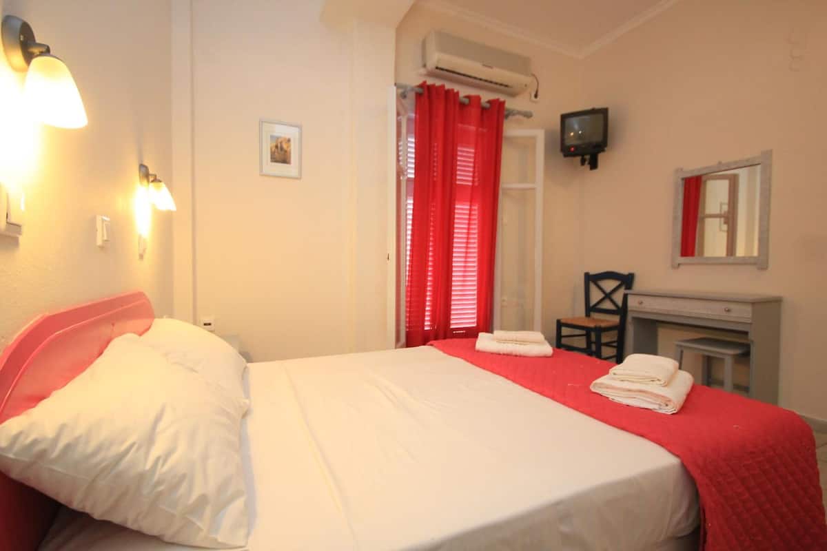 Habitación de hotel con cama, escritorio, silla, televisión y ventana con cortinas rojas.