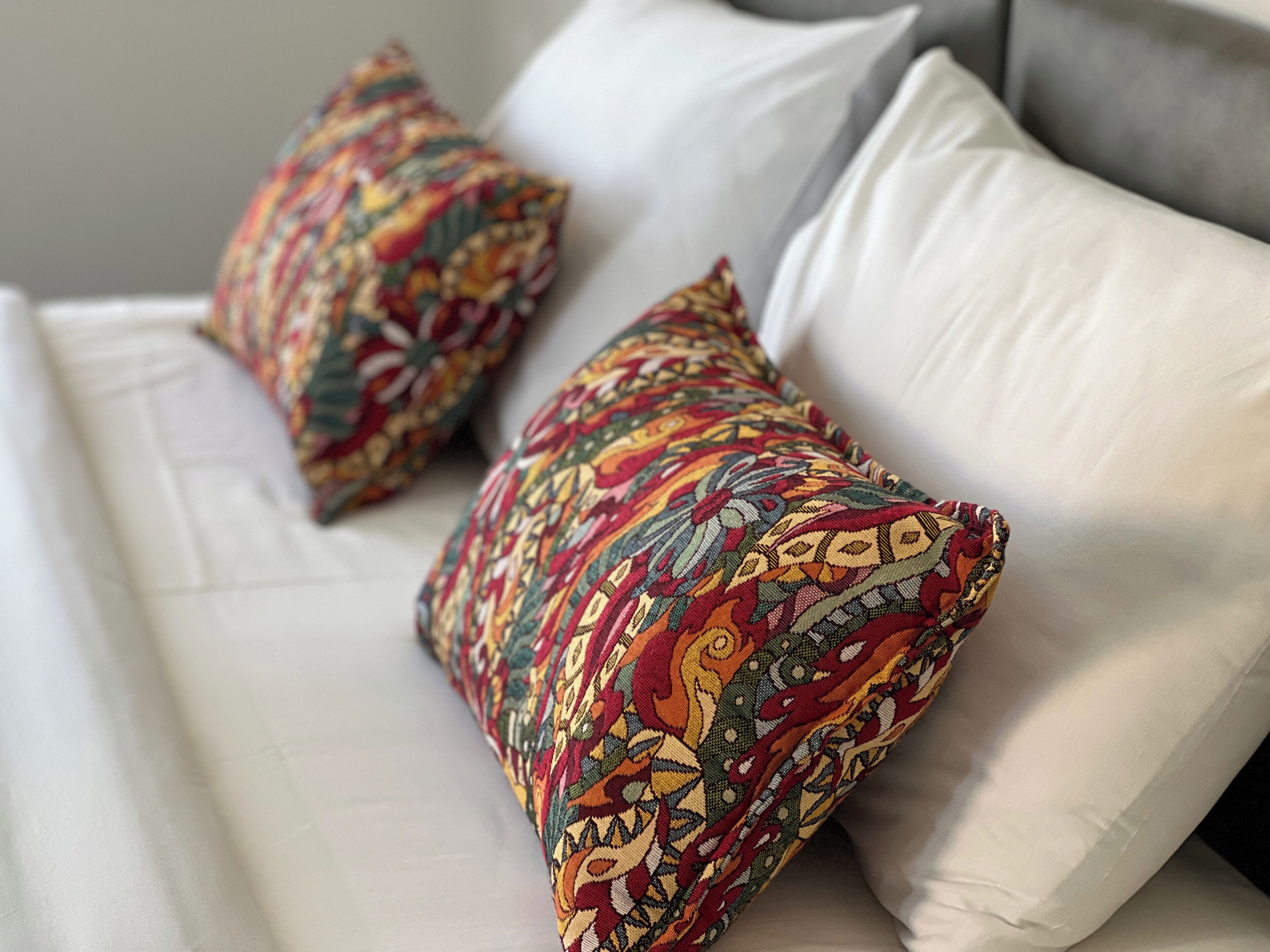 Un canapé blanc agrémenté de deux coussins décoratifs ornés d’un motif géométrique aux couleurs vives.