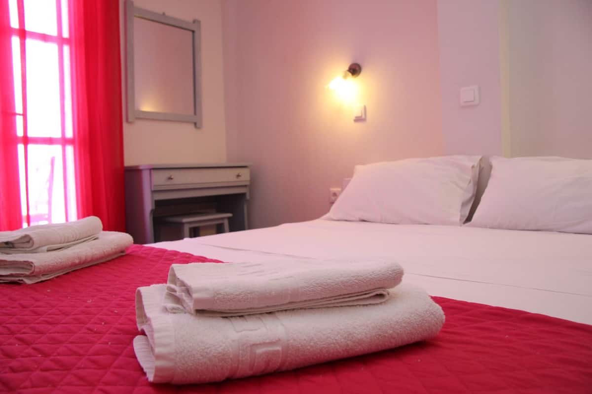 Habitación de hotel con cama, mesita de noche, espejo y lámpara de pared.