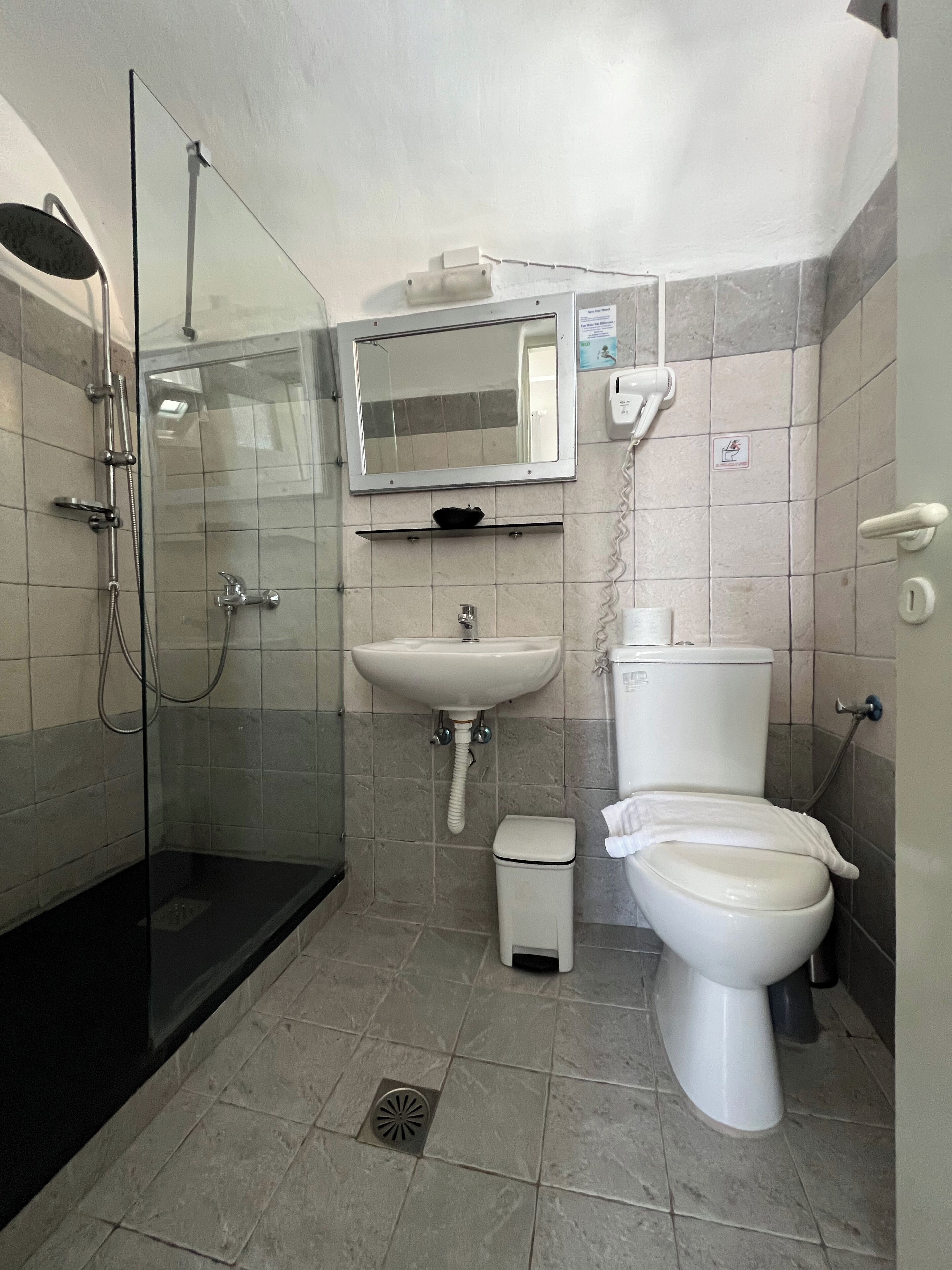 Une salle de bain avec une douche à parois de verre, un lavabo, des toilettes et une petite poubelle.