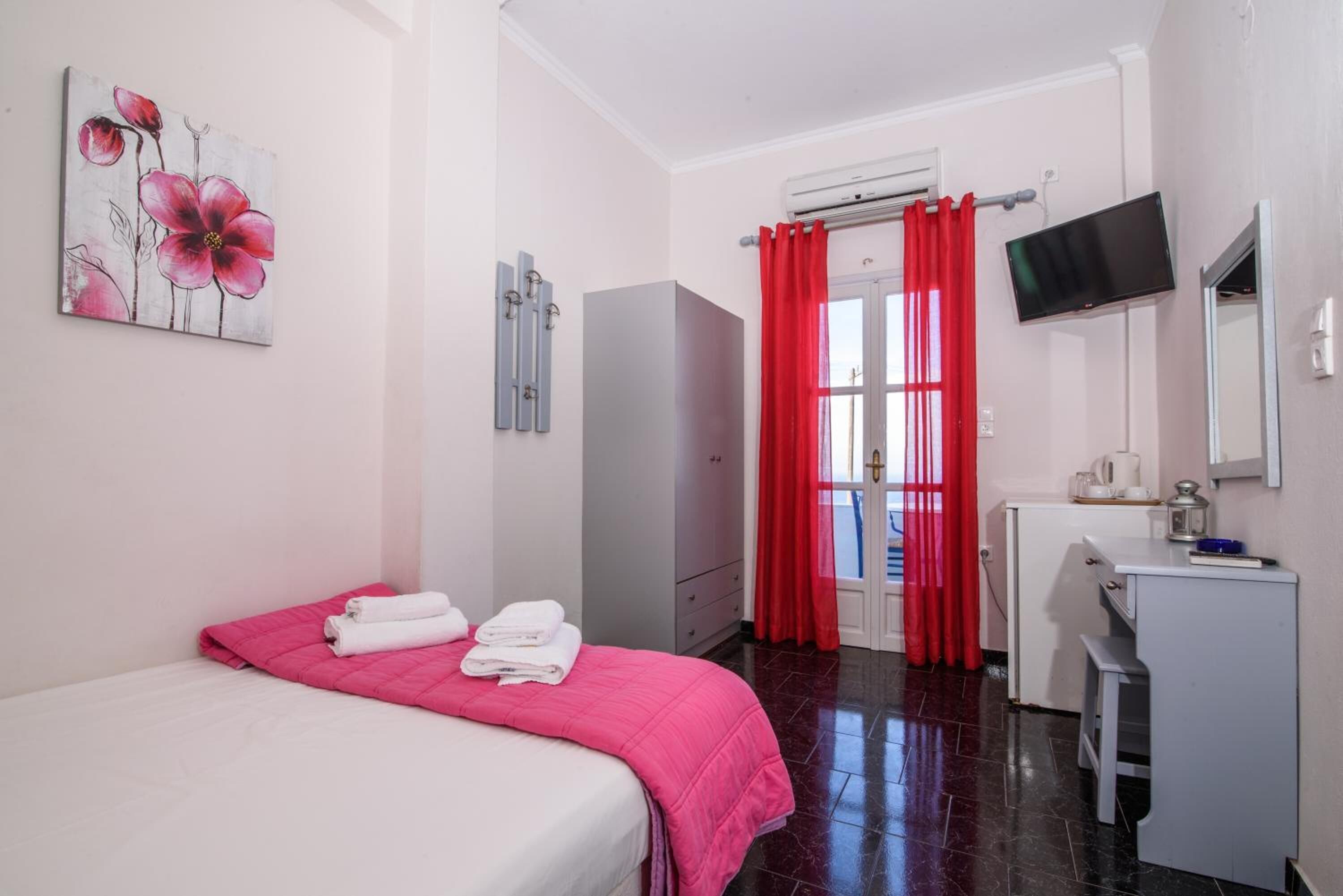 A hotel room with a bed, a desk, a TV, and a bathroom with red curtains.