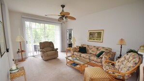 A living room with a beige armchair, a floral sofa, a wicker chair, a coffee table, and a ceiling fan.