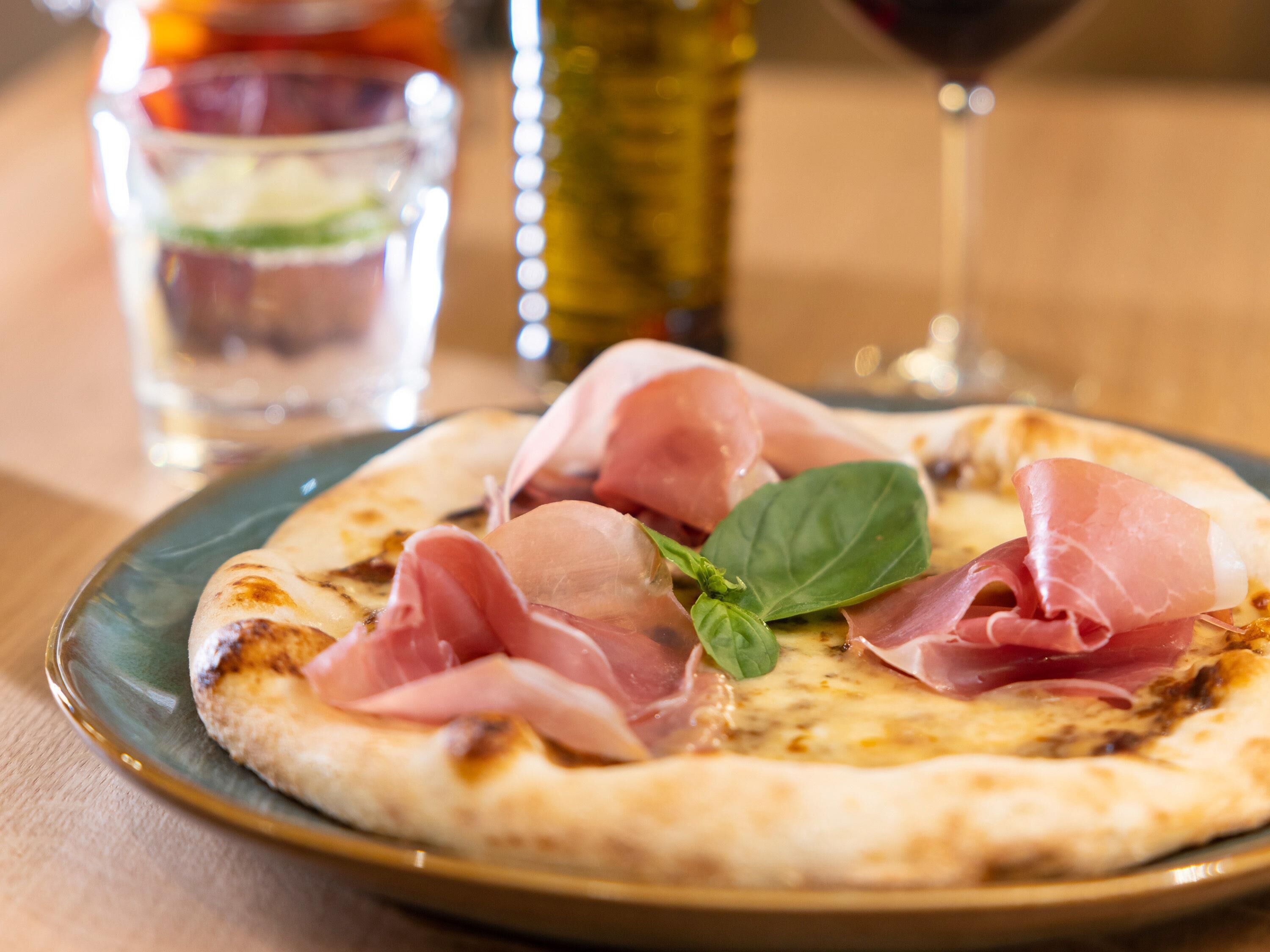 Une pizza à la garniture de jambon de Parme et de basilic, servie sur une assiette.