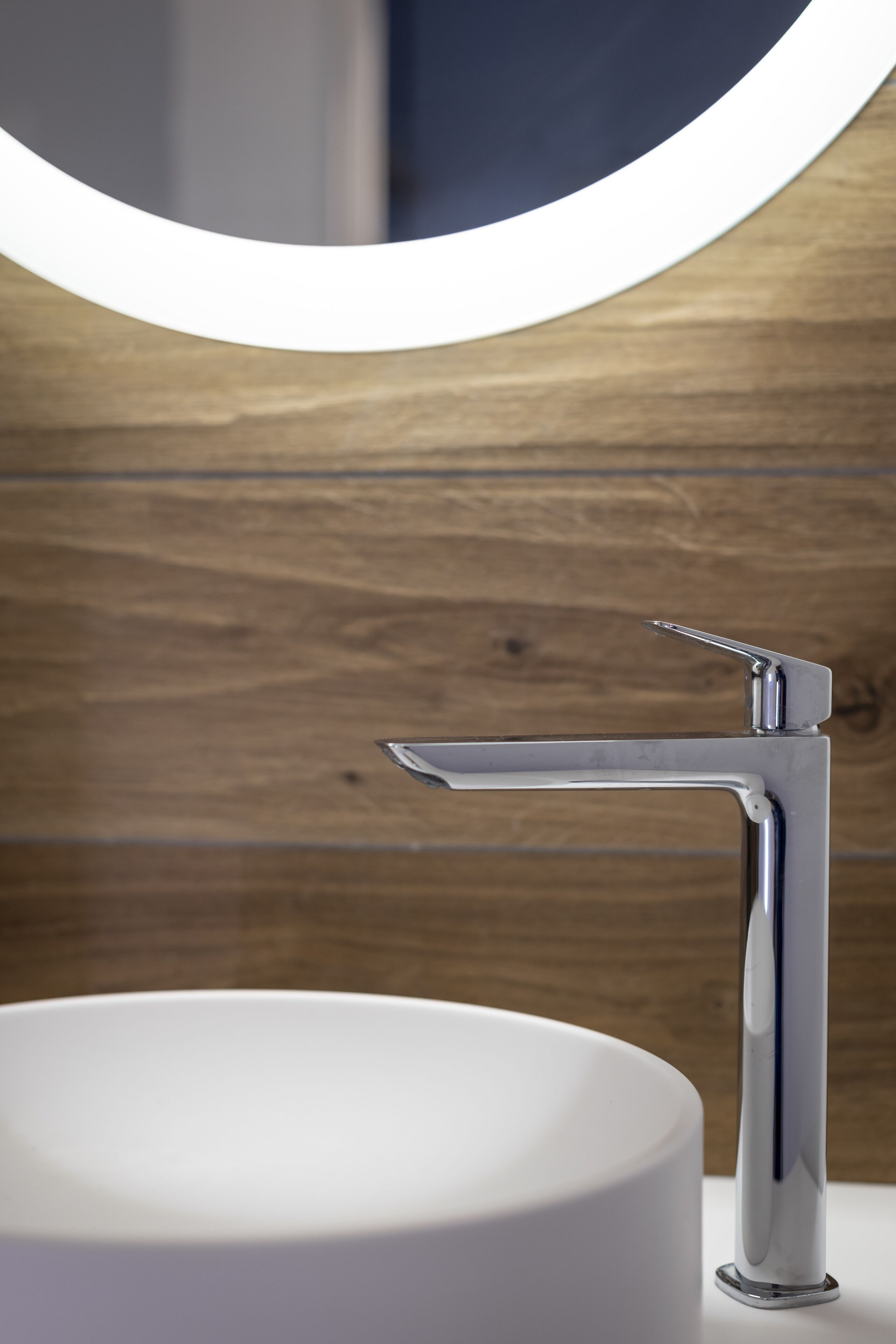 Un baño moderno con grifo de cromo y espejo redondo.