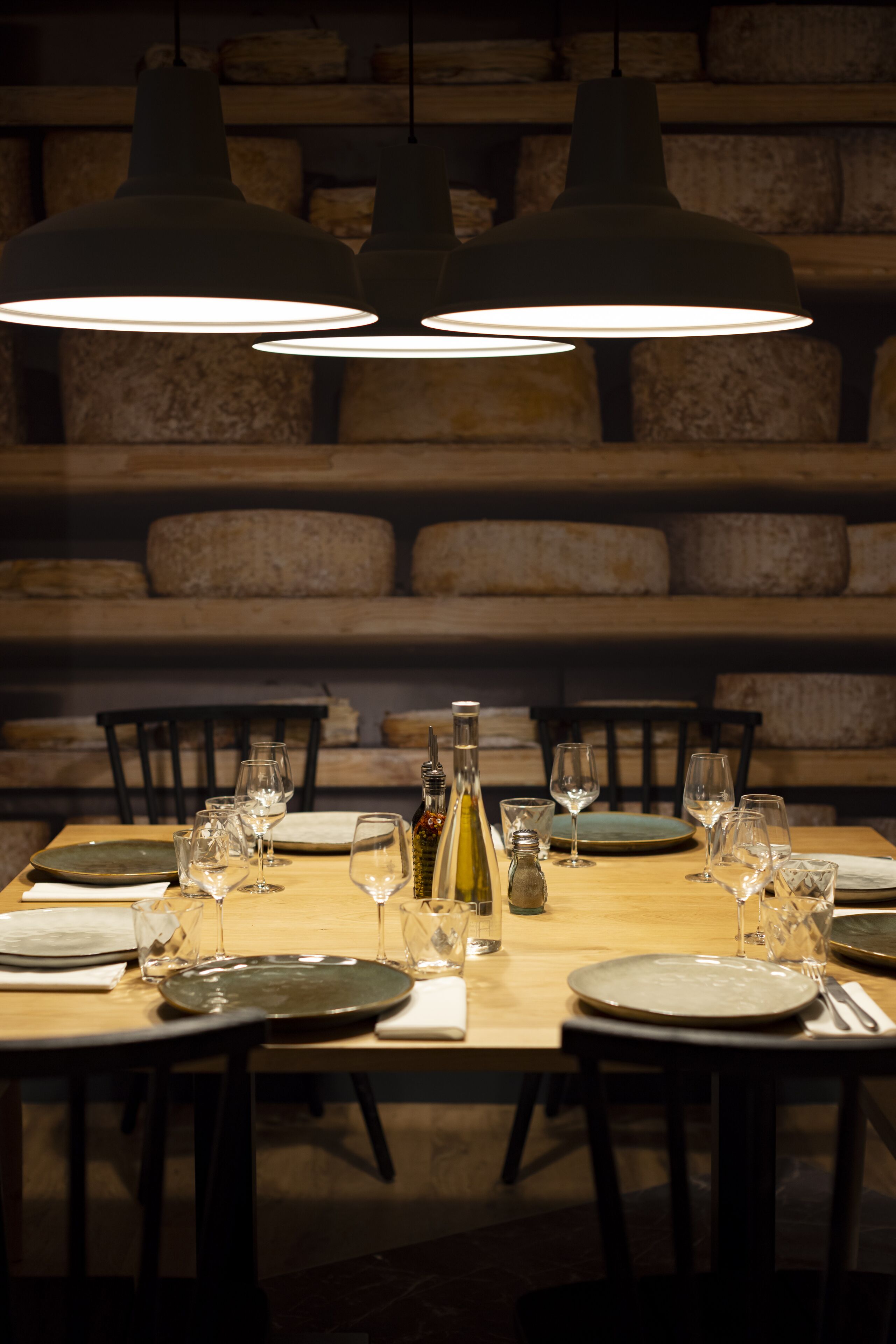 Une table à manger dressée avec des assiettes, des verres et une bouteille, et des lampes suspendues au-dessus.