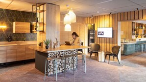 Zona de bar moderna con mostrador de madera, taburetes y una persona usando una computadora portátil.