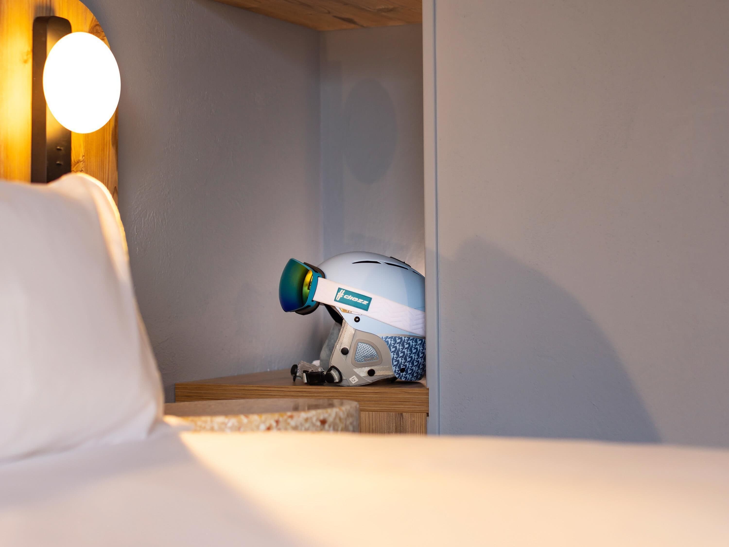 Un casco sobre una mesita de noche de madera con una lámpara fijada a la pared.