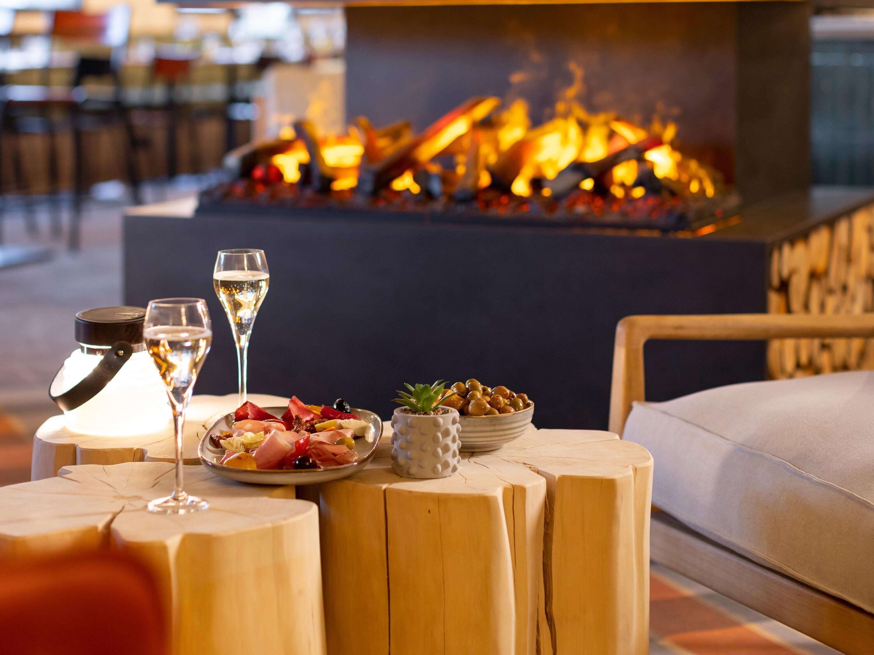 A cozy seating area with a wooden table, a plate of food, two glasses of wine, and a small potted plant.