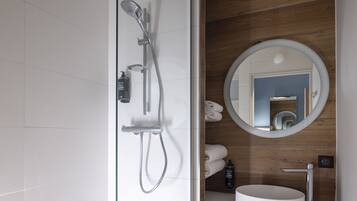 A modern bathroom with a glass-enclosed shower, a round mirror, and a white sink.