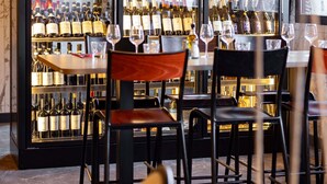 Zona de bar con varias botellas de vino y copas, sillas de madera y suelo de mármol.