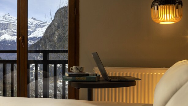Un dormitorio con vistas a montañas nevadas, una computadora portátil sobre una mesita de noche y una lámpara colgante.