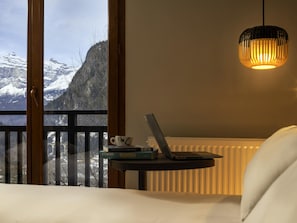 Un dormitorio con vistas a montañas nevadas, una computadora portátil sobre una mesita de noche y una lámpara colgante.