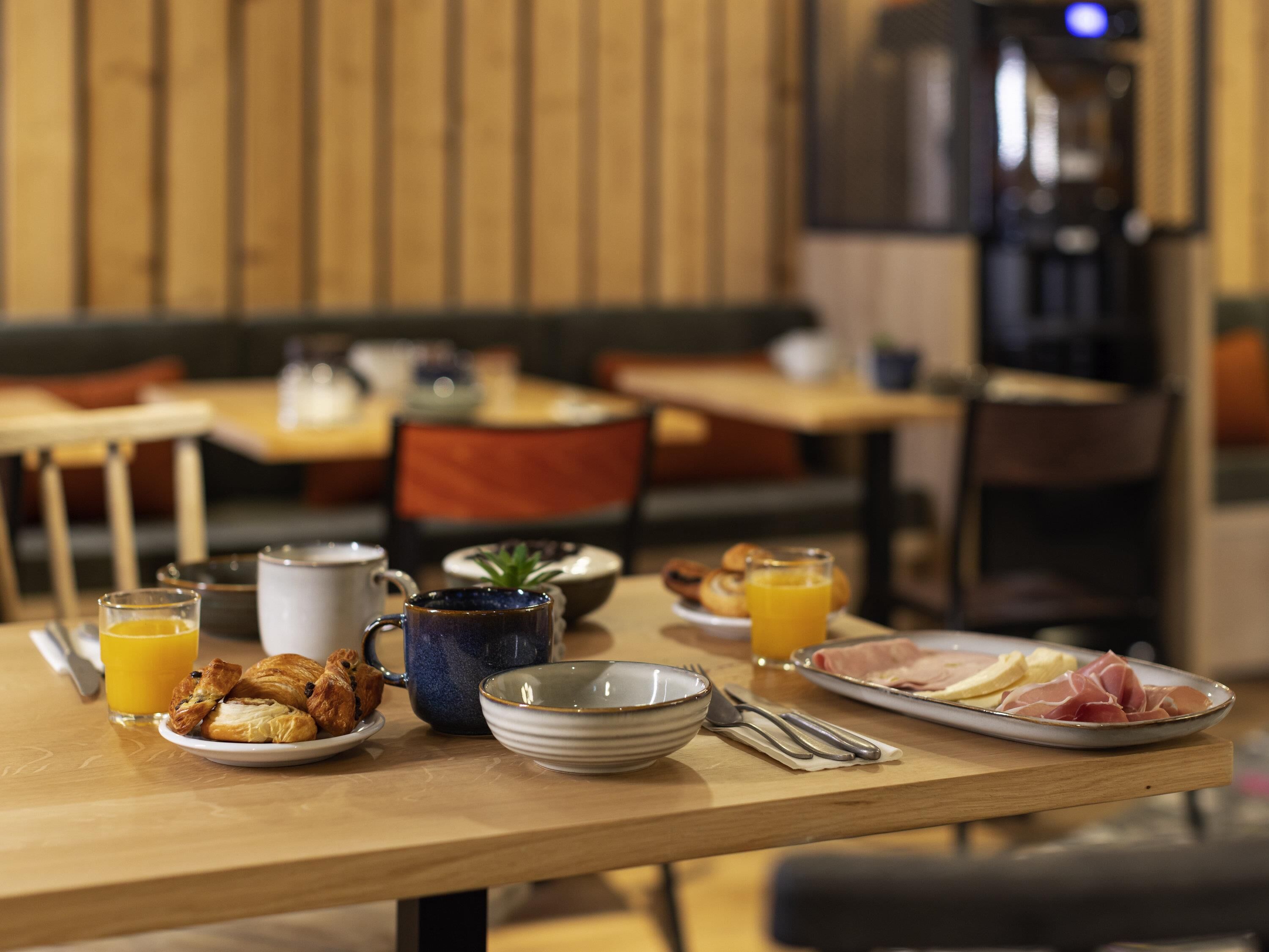 Una mesa de desayuno con croissants, zumo de naranja, una taza azul y un plato de jamón.