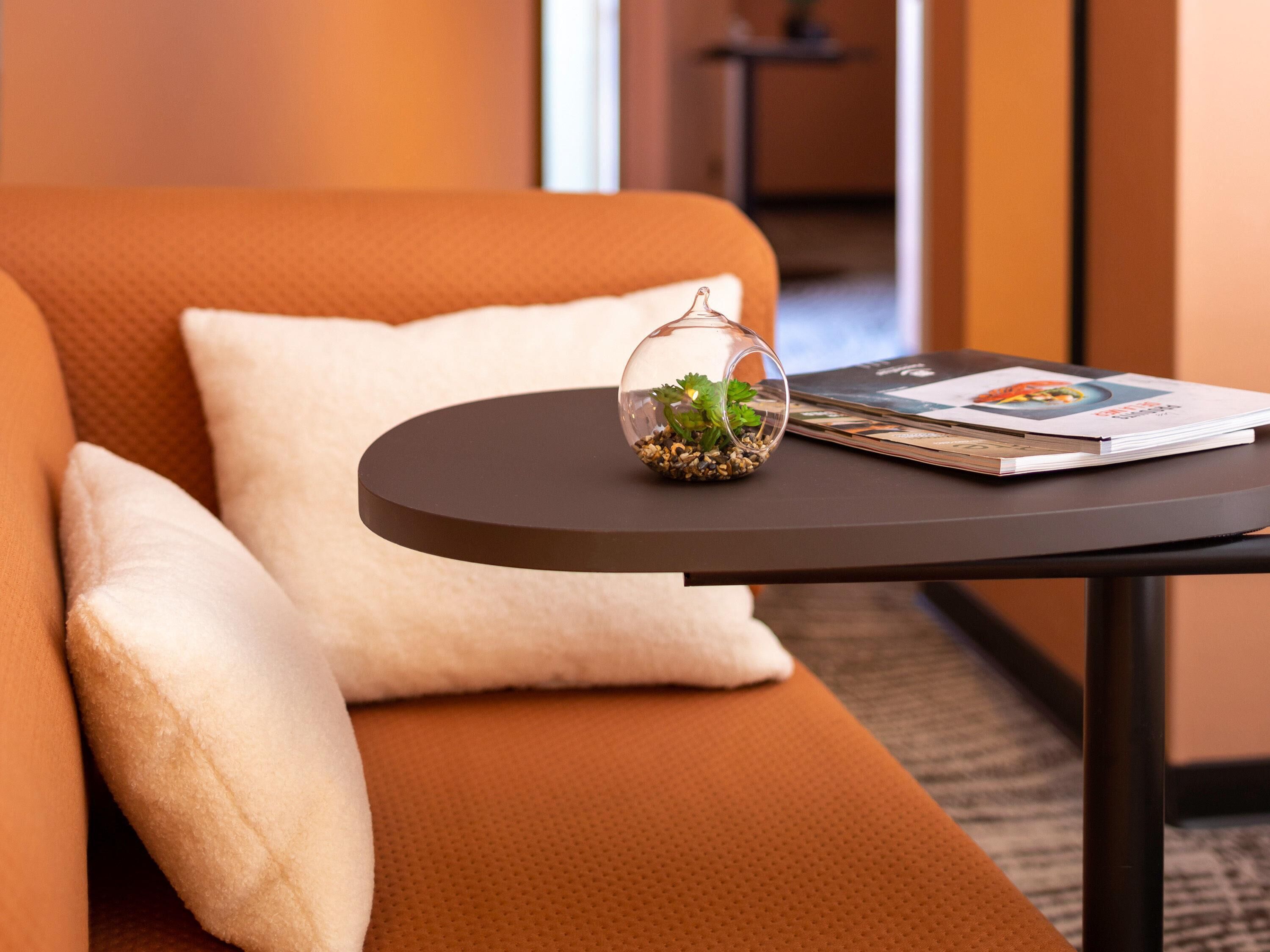 A modern hotel room with a round table, a glass terrarium, and a magazine.