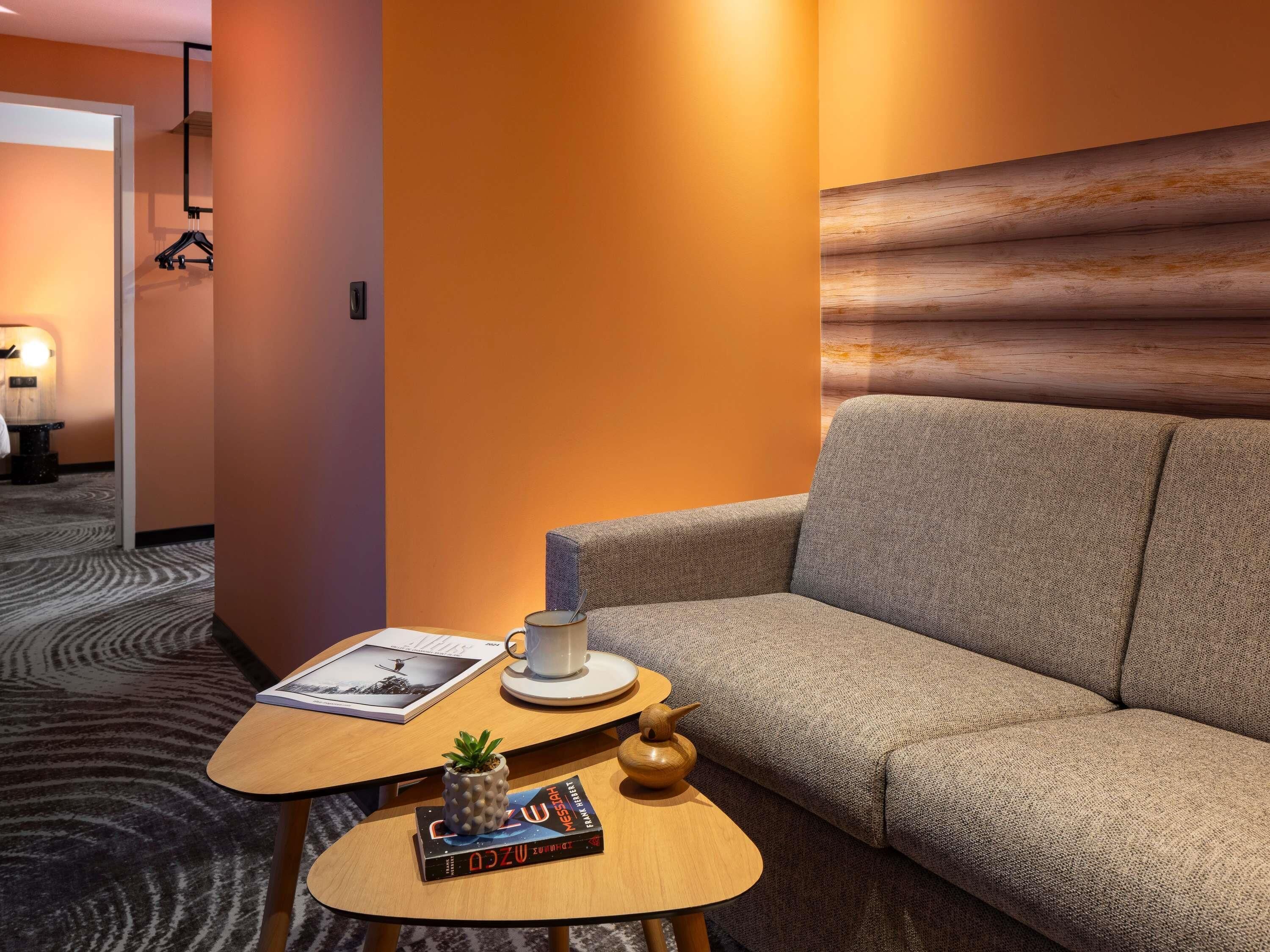 A hotel room with a sofa, a small wooden table, a cup, a book, and a small plant.