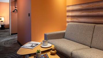 A hotel room with a sofa, a small wooden table, a cup, a book, and a small plant.