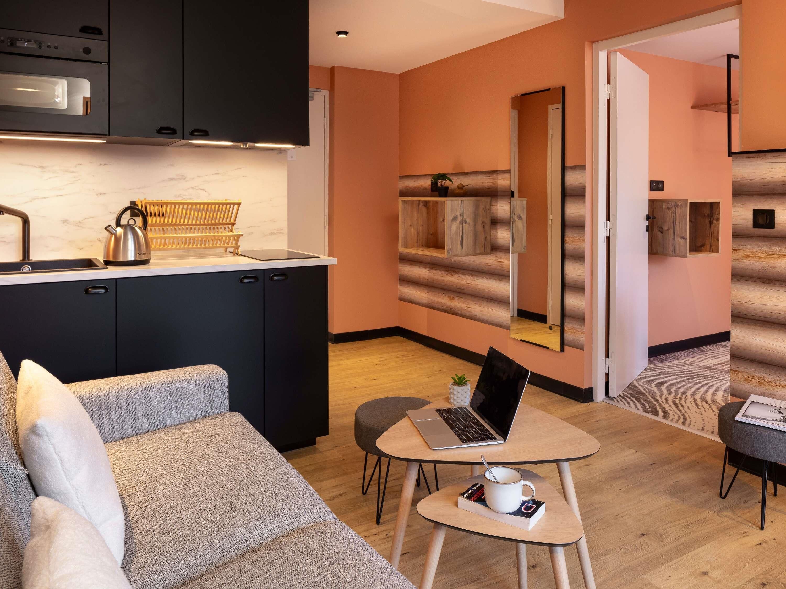 Une cuisine moderne avec des meubles de couleur sombre, un four encastré et un plan de travail sur lequel se trouvent une bouilloire et un présentoir en bois.