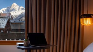 Habitación de hotel con cama, una laptop sobre una mesita y vistas a las montañas a través de la ventana.