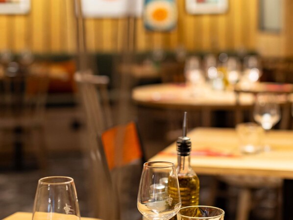 Un interior de restaurante con mesas preparadas para comer, una botella de vino y copas sobre la mesa.