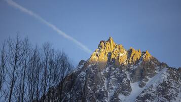 Un sommet de montagne enneigé, sous un ciel dégagé, avec une traînée de condensation bien visible.